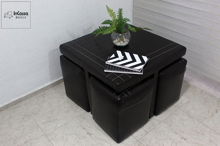 La imagen destaca el diseño compacto y funcional de la mesa de centro con taburetes incluidos, ideal para espacios pequeños. Su acabado en tacto piel negro y costuras decorativas aporta un toque elegante, perfecto para ambientes contemporáneos.