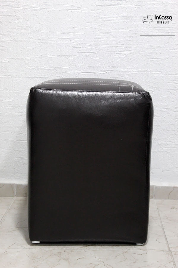 La foto destaca un taburete con acabado en tacto piel negro, diseñado para ofrecer comodidad y funcionalidad en espacios pequeños. Su estructura compacta lo convierte en una solución versátil para complementar salas, comedores o áreas de trabajo.