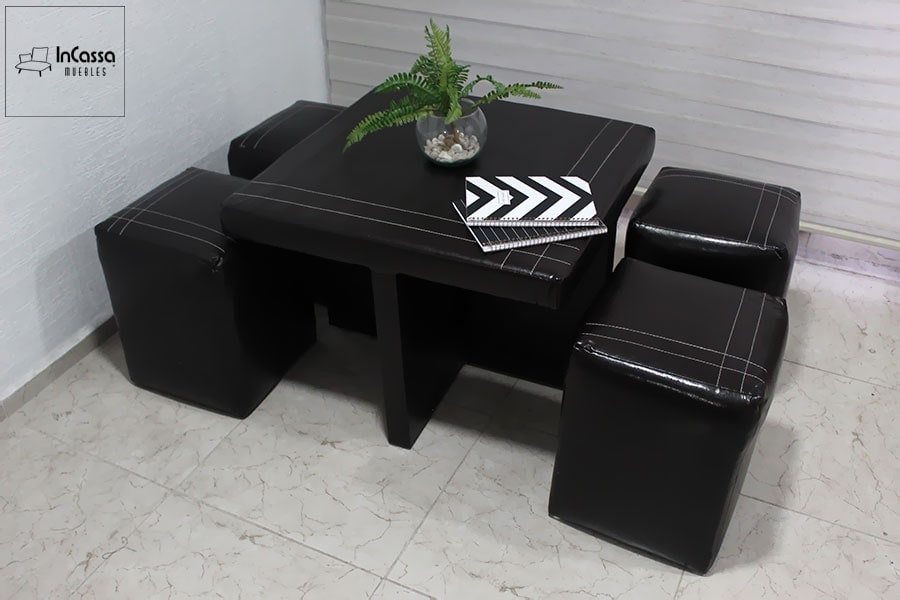 La foto muestra la mesa desde otra perspectiva, resaltando su funcionalidad como un mueble todo-en-uno. Cada taburete se acomoda de manera sencilla, permitiendo mantener el área organizada y libre de desorden. El set completo se encuentra tapizado en elegante tacto piel color negro.