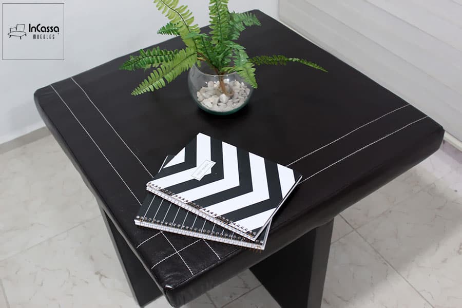 En esta imagen cercana se aprecia el elegante diseño de las costuras decorativas en la superficie de la mesa tapizada en tacto piel negro. Estos detalles destacan la atención al diseño y la calidad de la mesa.