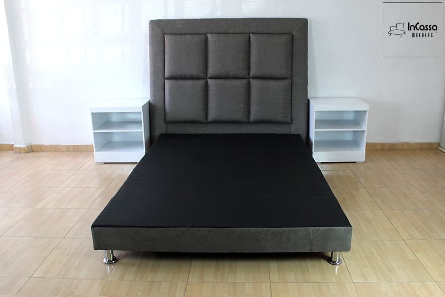 La foto presenta una vista frontal del juego de recámara con base tapizada en lino mouse, cabecera acolchada en bloques simétricos y burós blancos a cada lado. Las patas metálicas elevan la base, aportando un estilo moderno y funcional.