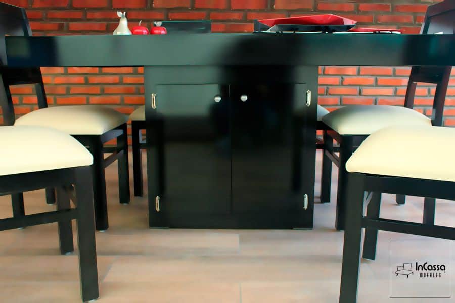 La imagen muestra el gabinete funcional ubicado en la base de la mesa del comedor, ideal para almacenar utensilios o manteles. El conjunto en tono chocolate resalta el contraste con los asientos tapizados en suede color hueso, aportando calidez y elegancia.