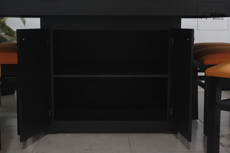 En esta vista se aprecia el interior del gabinete central, conformado por dos compartimentos amplios ideales para almacenar utensilios o mantelería. El acabado en color chocolate resalta la sobriedad del diseño, acompañado por las sillas tapizadas en suede tono naranja que aportan contraste y calidez.