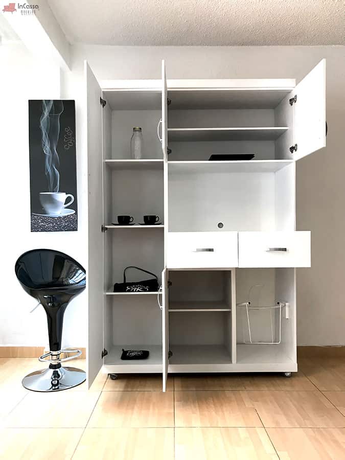 Toma frontal de la Alacena para Microondas MÁLAGA en acabado blanco, mostrando sus compartimentos abiertos con repisas ajustables, dos cajones centrales con jaladeras plateadas y espacios inferiores, incluyendo un canasto metálico lateral. La distribución permite almacenar utensilios, vajilla y accesorios de cocina de manera práctica y elegante.