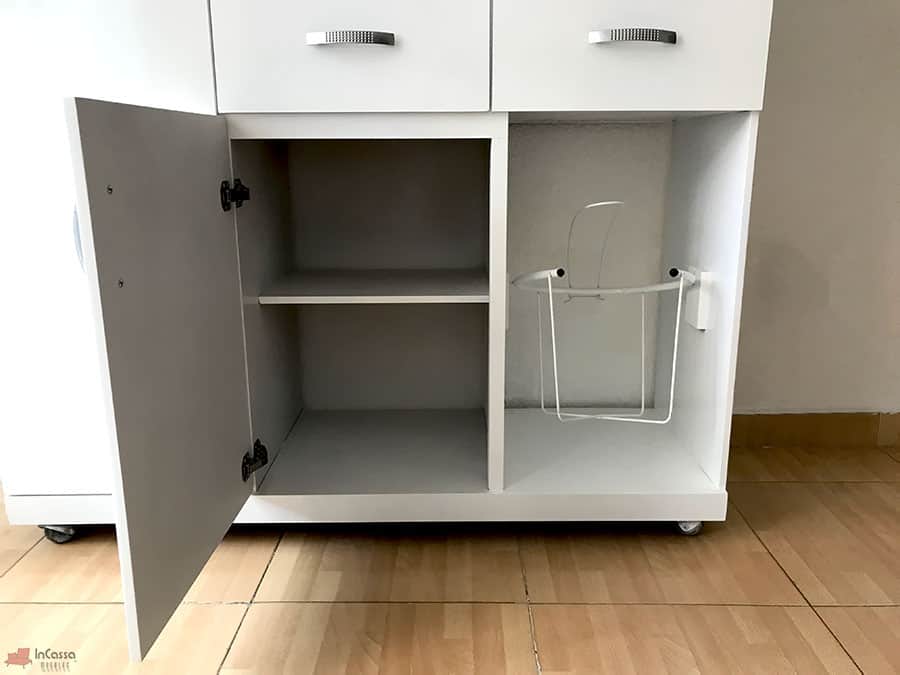 Imagen inferior de la Alacena para Microondas MÁLAGA en color blanco, mostrando a la izquierda un compartimento con repisa interna y puerta abatible, y a la derecha un espacio abierto con canasto metálico lateral ideal para almacenar bolsas o botellas. El diseño aprovecha al máximo el área de guardado.