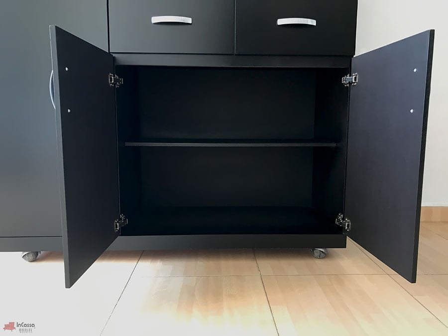 Se presenta la parte inferior de la Alacena para Microondas MÁLAGA en color chocolate mate, con ambas puertas abiertas y una repisa interna que divide el espacio en dos niveles. El diseño con bisagras metálicas y base con ruedas facilita su apertura y movilidad.