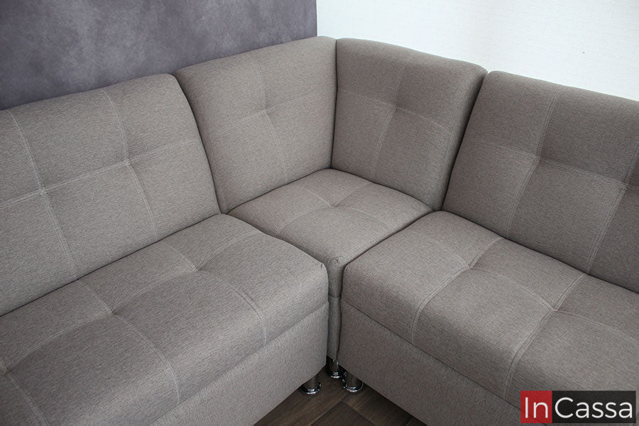 Podemos ver más de cerca el sillón esquinero y dos de los tres love seat que conforman la sala. La toma nos da una mejor imagen de los asientos así como de los respaldos además de algunas de las patas metálicas que sostienen los módulos, mismos que están tapizados en su totalidad por tela lino color greige con un acabado capitoneado.