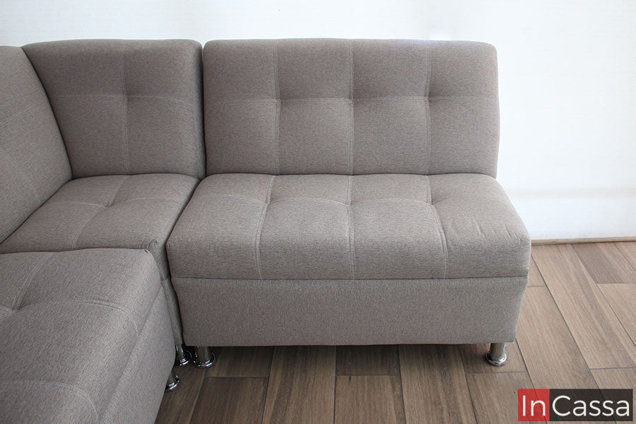 La foto se concentra principalmente en uno de los love seat, mostrando una toma completa de frente del mueble, donde podemos apreciar su respaldo y asiento tapizados en lino greige con acabado capitoneado, además de sus patas metálicas cromadas.