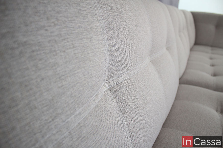 Una toma que nos proporciona una vista cercana de los respaldos y parte de los asientos de la sala, donde podemos apreciar más a detalle la textura de la tela lino en color greige, así como el terminado capitoneado presente tanto en los asientos como en los respaldos.