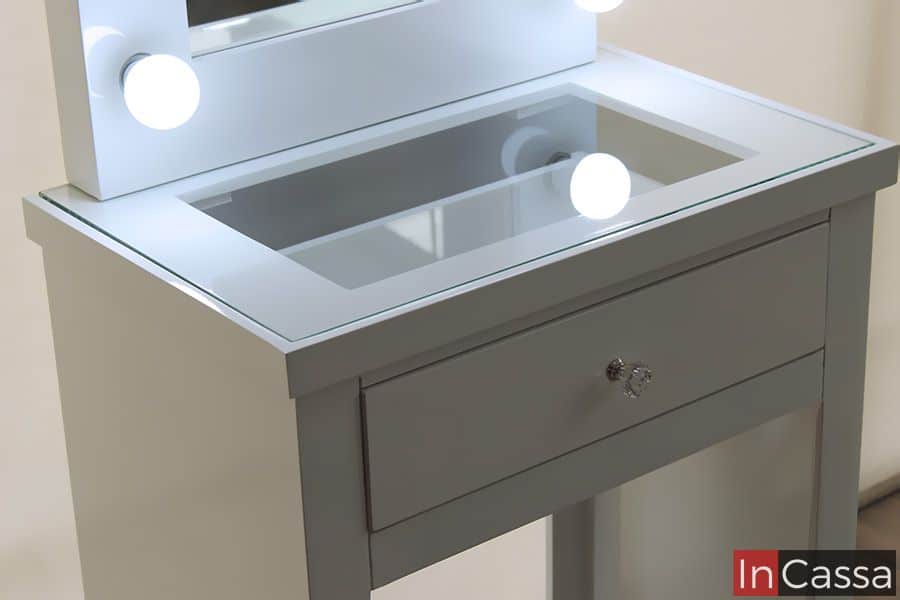 La foto presenta el elegante tocador blanco Manhattan con una superficie de vidrio templado, que permite visualizar el contenido del compartimento interior. Este diseño no solo añade un toque moderno, sino que también ofrece funcionalidad al mantener organizados los accesorios sin perderlos de vista.