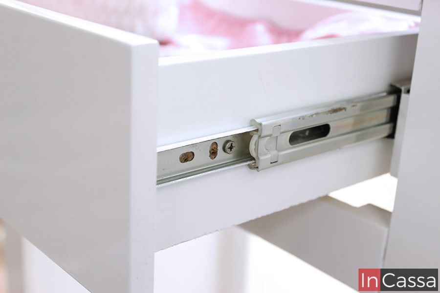 La imagen presenta el sistema de correderas metálicas laterales del tocador Manhattan, que garantiza un deslizamiento suave y seguro. Este herraje de calidad asegura la durabilidad y funcionalidad del cajón blanco, permitiendo un acceso cómodo a tus artículos de cuidado personal o maquillaje.