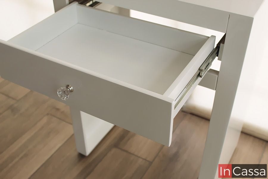 La foto presenta el tocador Manhattan desde un ángulo lateral, donde se aprecia su estructura estilizada y acabado blanco brillante. Este diseño minimalista es ideal para espacios pequeños sin sacrificar estilo ni funcionalidad.