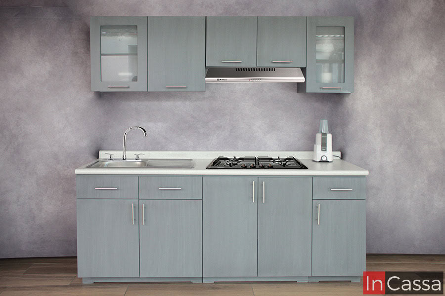 Se muestra la vista frontal completa de una cocina integral en tono gris cenizo claro, equipada con campana, tarja de acero inoxidable y parrilla empotrada. El diseño incluye módulos superiores con puertas de vidrio esmerilado y jaladeras metálicas.
