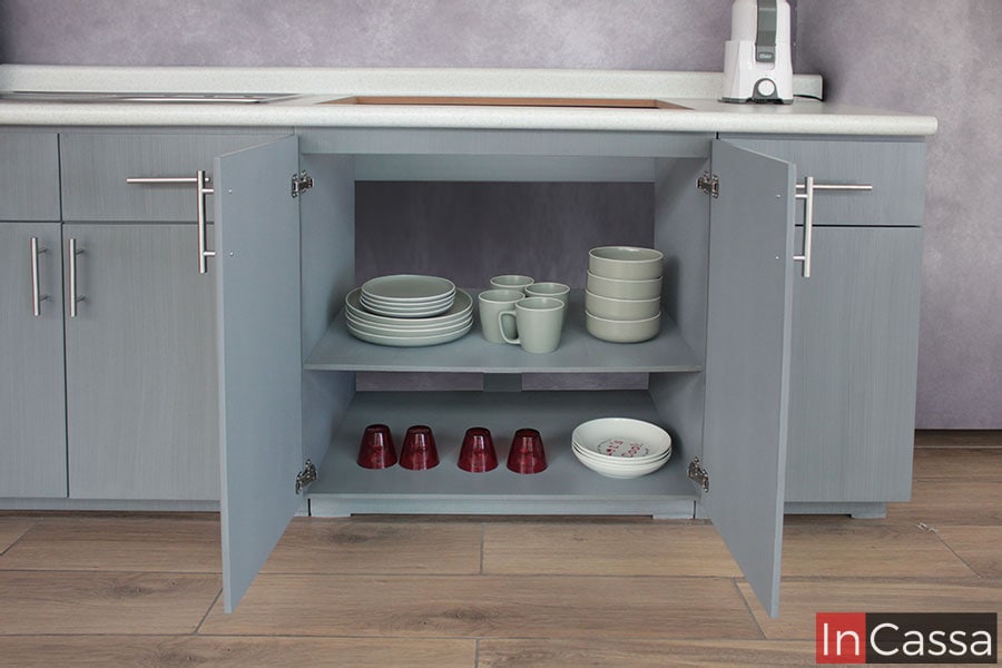 Una toma frontal muestra el interior de un módulo inferior con puertas abiertas, terminado en gris cenizo claro. En su interior, los compartimentos con entrepaño ofrecen amplio espacio de almacenamiento, ideal para vajillas, utensilios o despensa.
