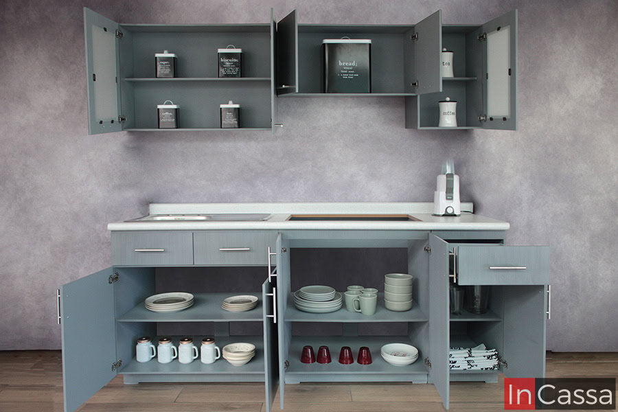 La imagen presenta todos los módulos de la cocina con puertas abiertas, revelando una excelente capacidad de almacenamiento. Se aprecian alacenas superiores con repisas y compartimentos para despensa, y gabinetes inferiores organizados para vajilla, utensilios y accesorios, todo en acabado gris cenizo claro completo.
