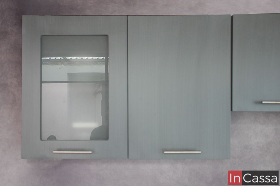 Se presenta una toma frontal de dos módulos superiores en acabado gris cenizo claro. Uno de ellos incluye puerta con vidrio esmerilado y jaladera metálica, resaltando el diseño moderno y funcional.