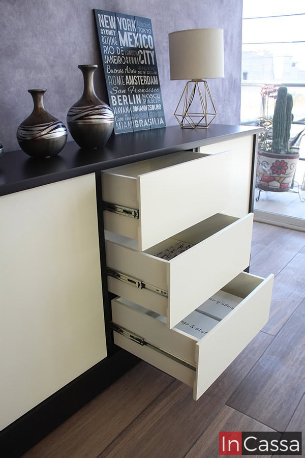 Una toma lateral del bufetero presentado con sus cajones abiertos, permitiéndonos apreciar la estructura completa de cada compartimento, en la que destaca su acabado blanco completo además de sus rieles metálicos integrados para la apertura y cierre de cada cajón.