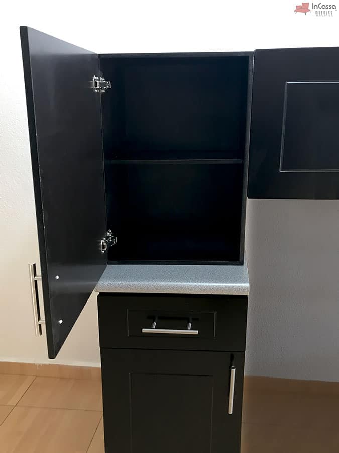 En esta toma se observa un módulo superior con puerta abierta que revela un entrepaño interno, ideal para organizar alimentos o utensilios. Justo debajo, el módulo inferior cuenta con un cajón funcional y un compartimento con puerta, todo en color chocolate con cubierta de formaica estilo granito purpina y jaladeras metálicas.