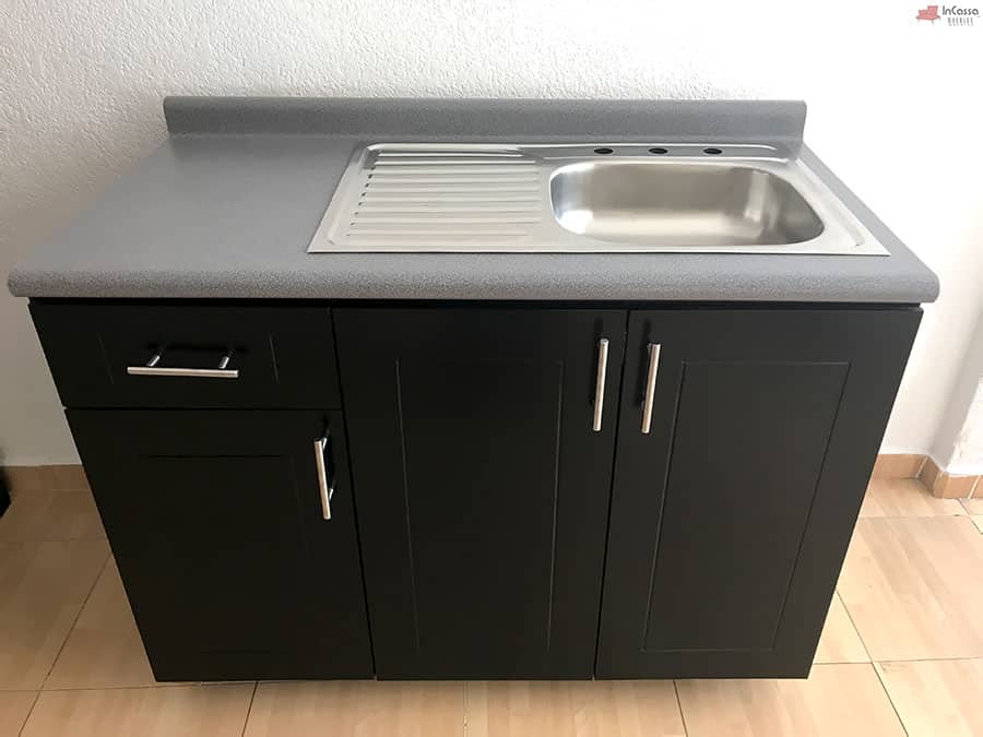 La foto presenta el módulo inferior de la cocina MCALLEN para estufa en color chocolate, equipado con tarja de acero inoxidable y escurridor integrado. Su cubierta en formaica granito purpina aporta resistencia y un acabado elegante, mientras que las puertas y cajón con jaladeras metálicas modernas completan un diseño práctico y funcional.