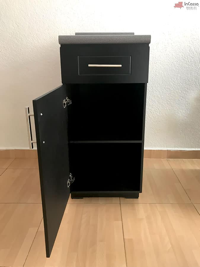 En la foto se aprecia el módulo inferior lateral de la cocina, fabricado en MDF color chocolate, con un cajón superior de correderas metálicas y un compartimento inferior de doble espacio gracias a su entrepaño. La cubierta de formaica estilo granito purpina aporta resistencia y elegancia, complementada con jaladeras metálicas modernas.