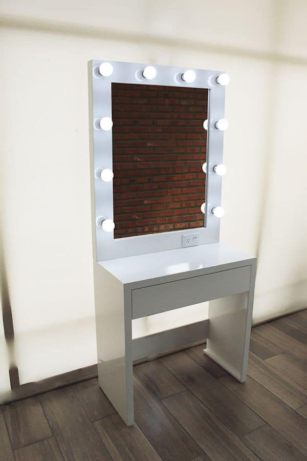 Tocador blanco minimalista con un espejo rodeado de luces LED brillantes, ideal para maquillaje y arreglo personal. El diseño limpio y moderno, combinado con una superficie amplia y un cajón de almacenamiento, crea un espacio funcional y elegante.