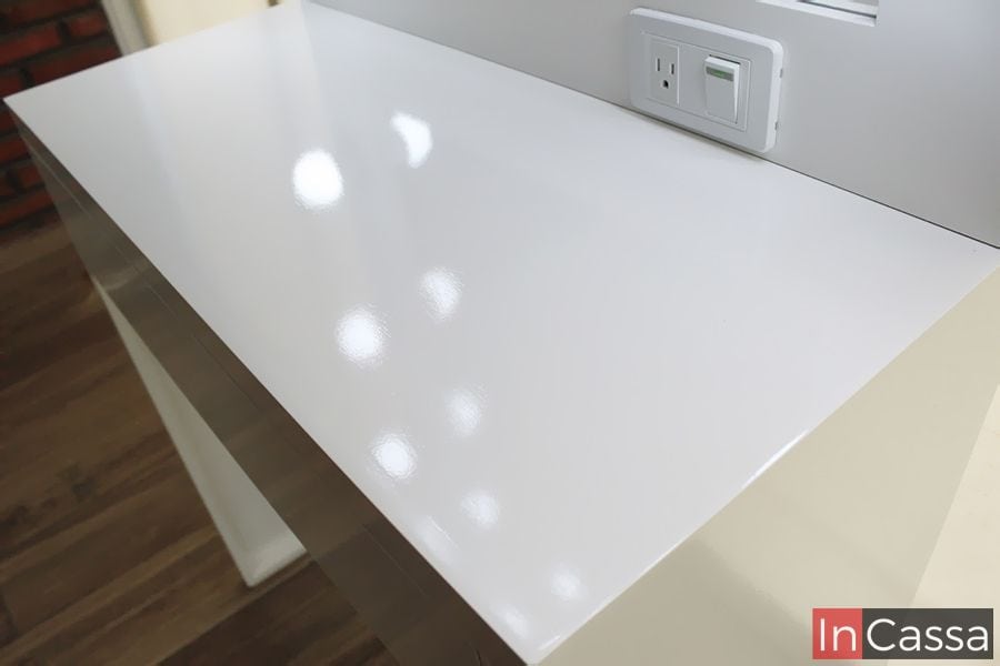 Detalle de la superficie brillante del tocador blanco minimalista. Incluye una práctica toma de corriente y un interruptor, ideal para conectar herramientas de belleza. El diseño limpio y moderno ofrece funcionalidad y estilo en cualquier espacio.