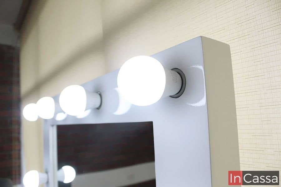 La foto muestra el detalle de las luces LED brillantes en el marco del espejo del tocador blanco. La iluminación resalta el diseño elegante y funcional del tocador, creando un ambiente ideal para el maquillaje y el cuidado personal.