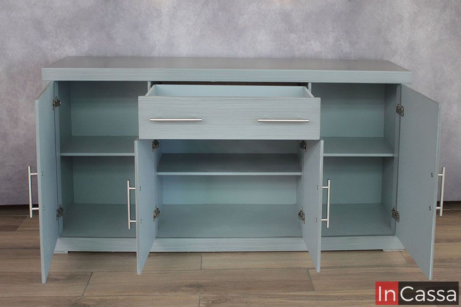 La foto presenta el Bufetero MISSISSIPPI totalmente abierto, mostrando su interior en gris cenizo claro y su excelente capacidad de organización. Se distinguen tres módulos con repisas amplias para vajilla, cristalería o utensilios, además de un cajón superior con correderas metálicas que desliza con suavidad. Las puertas abiertas permiten apreciar herrajes resistentes y jaladeras modernas que completan su diseño vintage–minimalista.