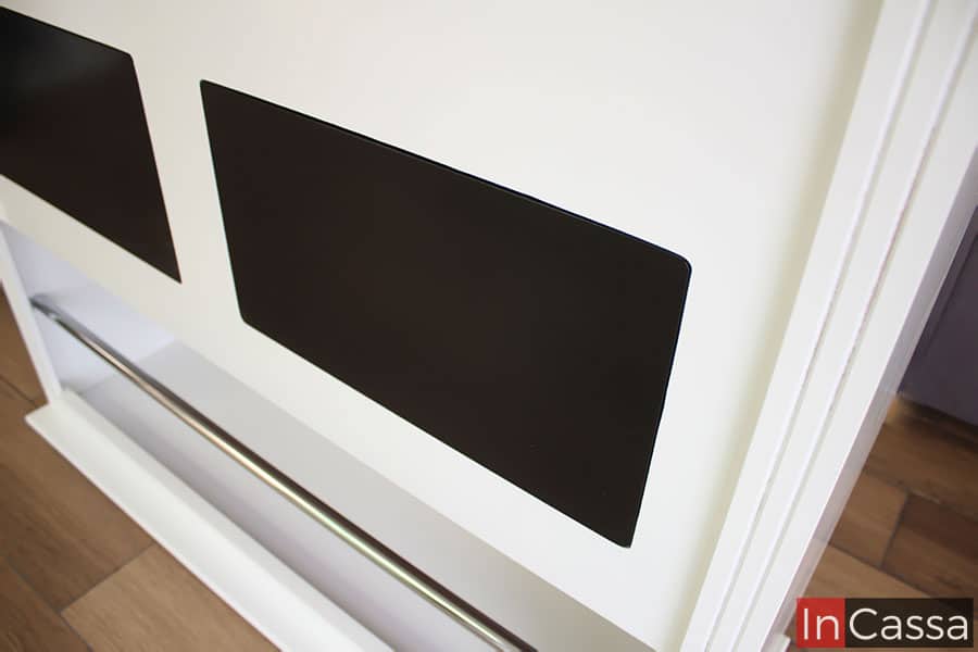 La foto se concentra en los detalles estéticos y funcionales en el diseño de la cantina, como son los dos parches decorativos en el frente del mueble los cuales le proporcionan variedad a su abundante tono blanco, además de que tenemos una vista cercana de la barra metálica que sirve como posa pies.