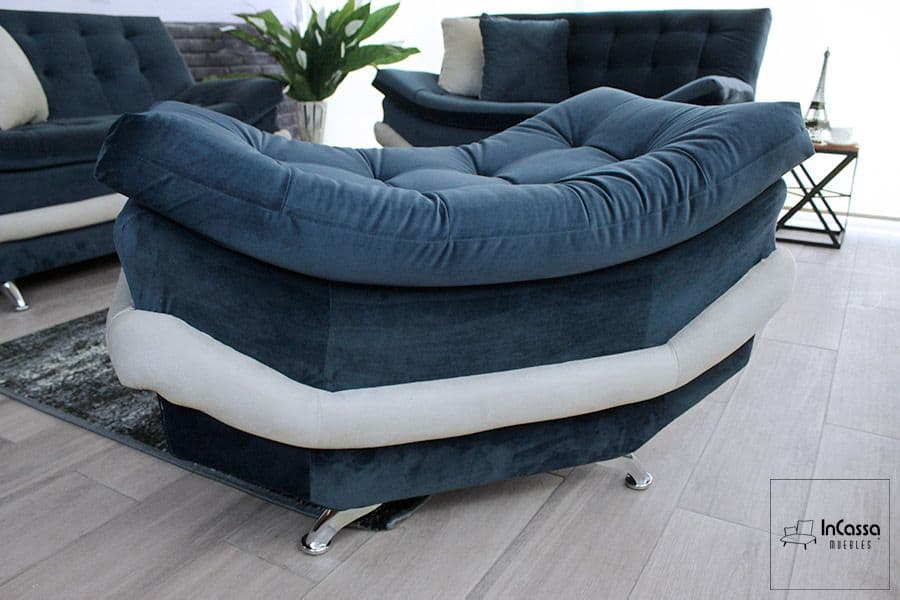 En esta toma se aprecia el taburete del modelo Murcia, tapizado en suede azul marino con acento hueso. Su forma curva y acolchonada, junto con el acabado capitonado, transmite una sensación de suavidad y confort. Las patas metálicas cromadas completan su diseño contemporáneo, ideal para complementar la sala con estilo y armonía visual.