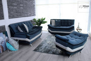 La imagen muestra la Sala Modelo Murcia en un elegante tapizado de suede azul marino, compuesta por dos love seat y un taburete. Su diseño moderno de líneas suaves y costuras capitonadas resalta sobre un ambiente contemporáneo con muros de ladrillo gris y piso tipo madera, creando una atmósfera acogedora y sofisticada ideal para cualquier estancia.