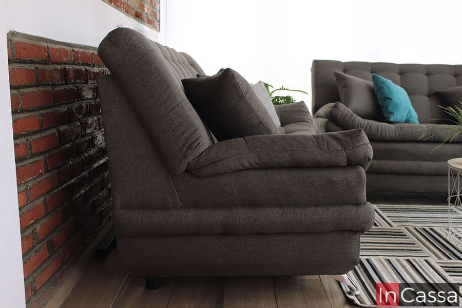 La fotografía muestra un love seat del modelo Murcia en tapizado lino mouse, capturado desde un ángulo lateral que destaca su perfil acolchado y respaldo ergonómico. Los cojines decorativos aportan suavidad visual, mientras las costuras capitonadas y la doble capa de asiento evidencian su diseño confortable y moderno, ideal para interiores contemporáneos.
