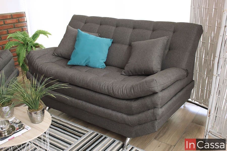 La imagen presenta el love seat del modelo Murcia, tapizado en elegante lino color Mouse, un tono gris cálido que realza su diseño contemporáneo. El capitonado profundo del respaldo y los cojines contrastantes en gris y turquesa aportan textura y frescura al espacio. Sus suaves líneas curvas y patas cromadas completan una estética moderna, perfecta para ambientes sofisticados y acogedores.