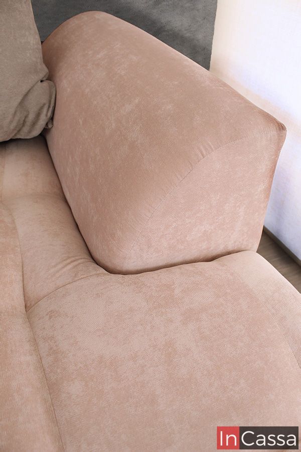 Una toma cerrada resalta el brazo curvo de la sala en tapiz suede rosa palo. La textura suave tipo velvet y el acolchado voluminoso ofrecen un diseño ergonómico y elegante, ideal para espacios modernos y confortables.