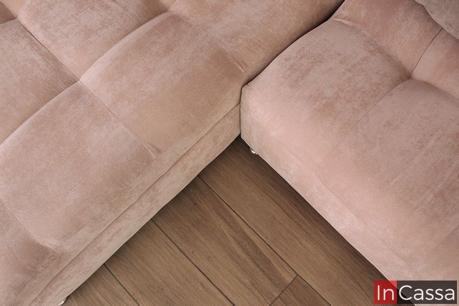 Una toma superior detalla la unión de los módulos en esquina de la sala tapizada en suede rosa palo, mostrando la perfecta alineación de costuras y el acabado aterciopelado. El piso tipo madera refuerza la calidez y estilo acogedor del espacio.