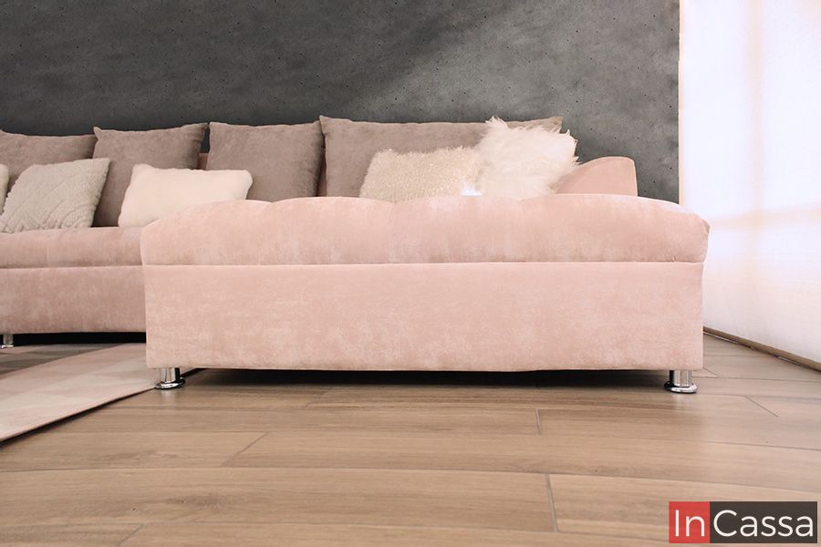La imagen captura el chaise longue lateral derecho de la sala esquinera en tapiz suede rosa palo, con textura aterciopelada y patas metálicas. Los cojines blancos de felpa y el fondo gris aportan contraste, mientras que la luz natural realza la suavidad del tapizado.
