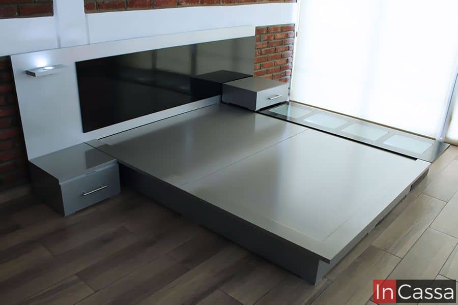 Cama moderna en tonos grises con cabecera y burós integrados. Diseño minimalista y elegante, incluye iluminación LED y una repisa funcional. Ideal para un dormitorio contemporáneo, ofreciendo estilo y practicidad.