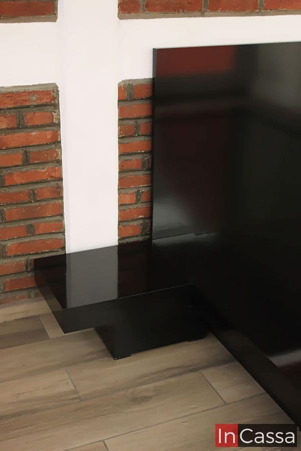 La foto presenta un primer plano del buró integrado al costado izquierdo de la cama, con una estructura en forma de “L” escalonada que le da un toque moderno. Su acabado negro brillante resalta sobre el muro de ladrillo, añadiendo sofisticación y contraste visual al ambiente.