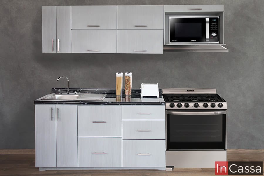 Moderna cocina integral diseñada para estufa de piso instalada en una pared gris. Todos los módulos de la cocina tienen un acabado gris cenizo claro, además el módulo inferior largo cuenta con una cubierta de formaica de color negro. Cabe destacar que los módulos superiores ofrecen un espacio para microondas.