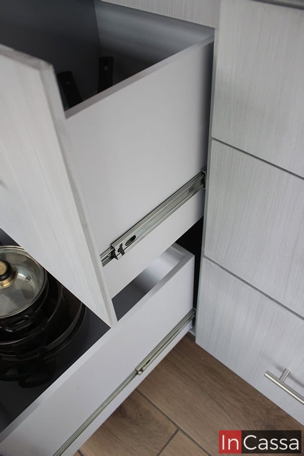 Una imagen que ofrece una toma cercana de los cajones centrales del módulo inferior, destacando sus rieles metálicos integrados, mismos que conforman su sistema de apertura y cierre. También tenemos una vista parcial de los interiores de cada cajón, los cuales son bastante profundos y espaciosos, además de que mantienen el mismo tono, gris cenizo claro, en la totalidad de su estructura.