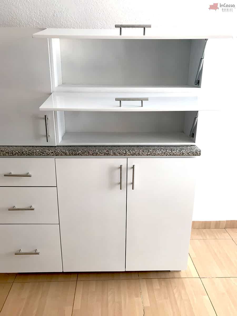 La imagen muestra una toma frontal de la alacena superior abatible de la Cocina Integral NEVADA de 2 metros en acabado blanco, con ambas puertas elevadas gracias a pistones metálicos que facilitan su apertura. El interior ofrece dos compartimentos amplios y luminosos, mientras que en la parte inferior se aprecia la cubierta de formaica estilo granito purpina junto con los módulos inferiores con frentes blancos y jaladeras metálicas que completan el diseño moderno y minimalista.