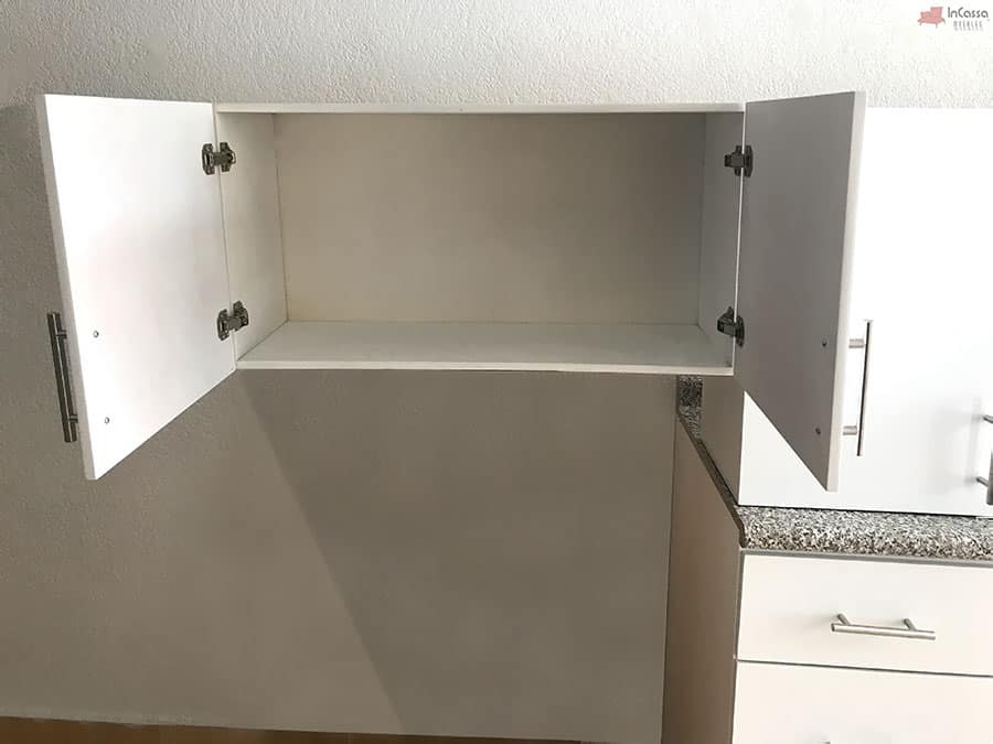 Una fotografía del mueble sobre campana de la Cocina Integral NEVADA de 2 m en acabado blanco, mostrada completamente abierta para destacar su interior amplio y uniforme. La toma resalta las bisagras metálicas, el diseño limpio y la superficie lista para almacenar vajilla, despensa o utensilios, en perfecta armonía con la cubierta estilo granito purpina situada debajo.