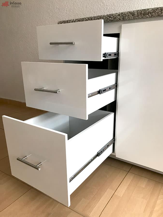 La foto presenta una toma lateral de los tres cajones de la Cocina Integral NEVADA de 2 metros, todos abiertos para mostrar su capacidad interna y sus correderas metálicas de extensión completa. Los frentes blancos con jaladeras de acero combinan con la cubierta de formaica estilo granito purpina, destacando un diseño limpio, moderno y altamente funcional.