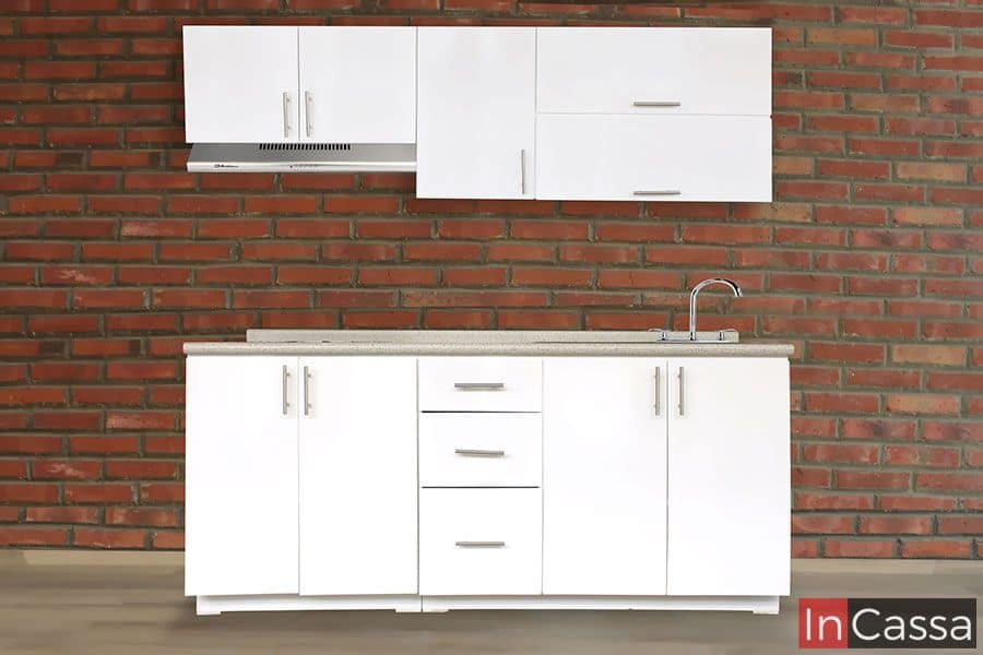 Moderna Cocina diseñada para parrilla de color blanco con cubierta de formica color granito de arena; las puertas y cajones cuentan con jaladeras metálicas con estilo "T". La cocina se encuentra instalada en una pared construida de ladrillo.