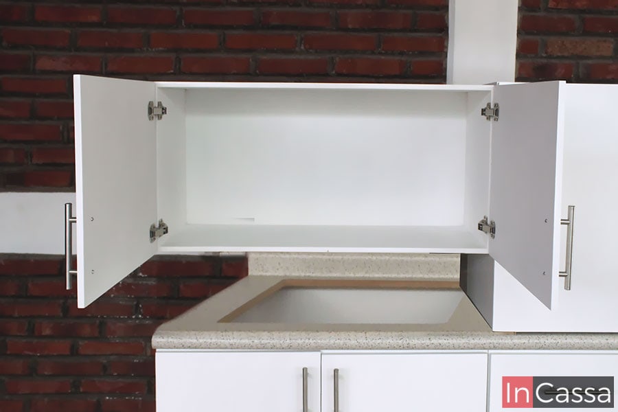 Una imagen con una toma cercana al mueble sobre campana de la cocina con sus puertas abiertas, mostrando un amplio espacio pintado en color blanco al igual que la estructura externa del módulo. También es posible ver las bisagras metálicas de las puertas, e incluso parte del módulo inferior, especialmente la sección del hueco para parrilla.