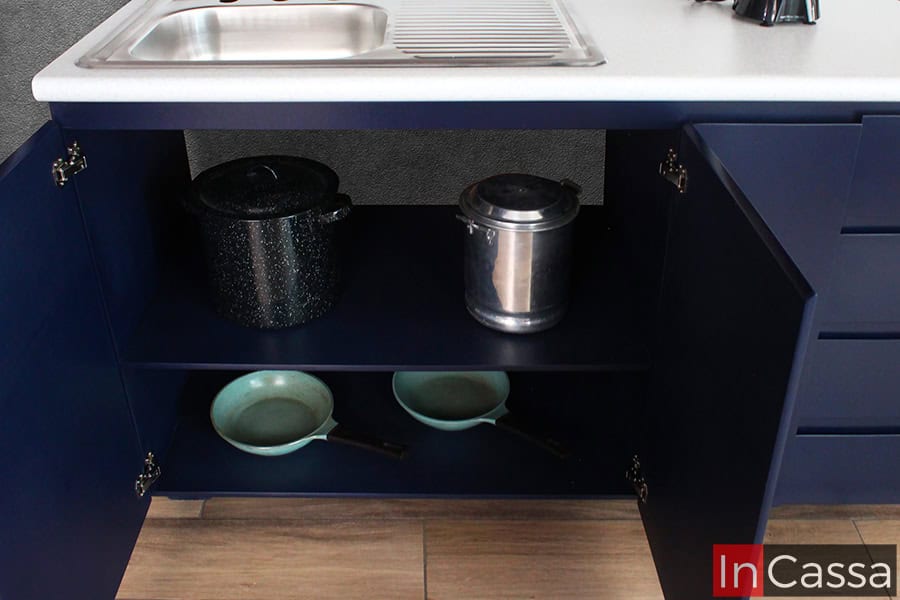 La imagen presenta el módulo inferior ubicado debajo de la tarja en la Cocina NICARAGUA para parrilla, con puertas abiertas que revelan dos amplios compartimentos. El área es ideal para guardar ollas, sartenes y utensilios voluminosos, manteniéndolos fuera de la vista pero fácilmente accesibles. El acabado azul rey resalta el estilo moderno y sobrio del conjunto.