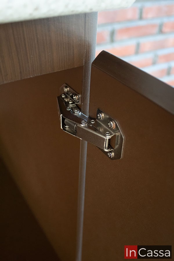 Foto de una de las muchas bisagras metálicas presentes en cada una de las puertas para su apertura y cierre, en la que además puede apreciarse parte de los interiores del módulo en color café, mientras que sus exteriores muestran una acabado tabaco laqueado.