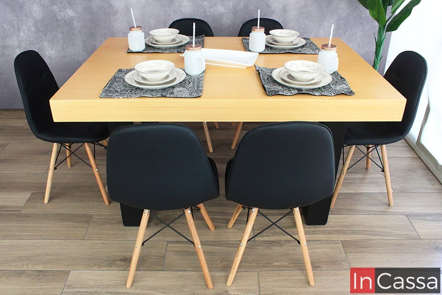 La imagen presenta una toma directa del comedor NORMANDÍA para seis personas, destacando la robustez de su cubierta en tono natural y la base de MDF negra. Las sillas tipo eames, con estructura en madera y asiento negro, enmarcan un diseño vanguardista y elegante.