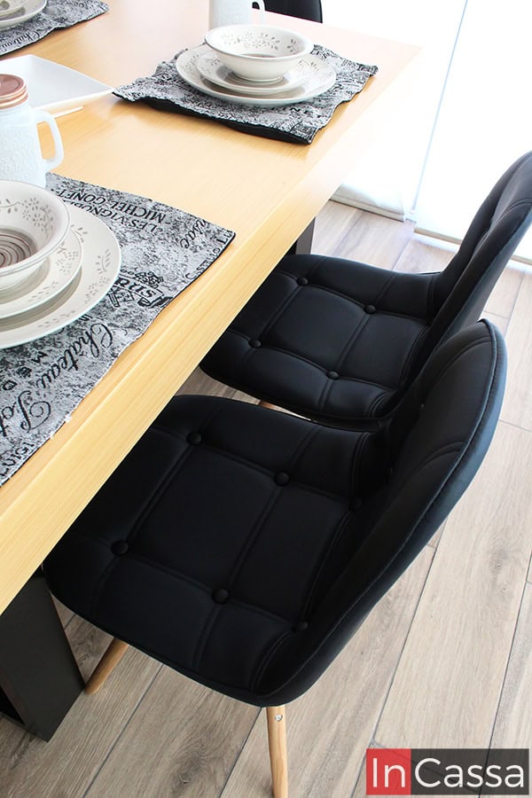 La fotografía destaca de cerca las elegantes sillas negras del comedor NORMANDÍA, mostrando su diseño capitonado y base de madera estilo nórdico. El contraste con la cubierta de tono natural realza su estilo industrial y moderno, ideal para espacios contemporáneos.