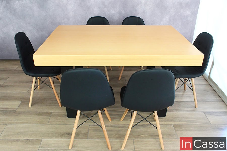 La imagen presenta una vista frontal del Comedor NORMANDÍA, donde destaca la cubierta de MDF en tono natural con un grosor robusto y elegante. Las seis sillas tipo eames en color negro se alinean perfectamente alrededor de la mesa, brindando un contraste visual moderno y sofisticado. Las patas en madera natural con estructura metálica aportan estabilidad y un estilo nórdico industrial, mientras que el pedestal industrial negro refuerza su diseño contemporáneo.